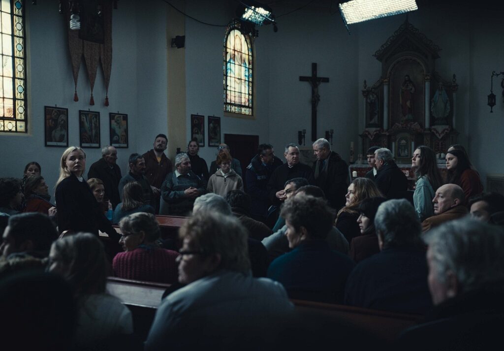 Asamblea en una iglesia, presidida por la cruz, para decidir si expulsar del pueblo a tres inmigrantes